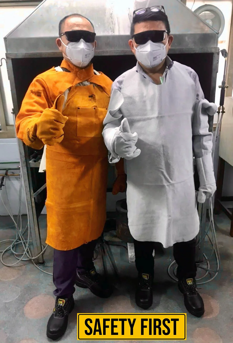 Two Amanda employees in full protective safety gear giving a thumbs up in the workshop