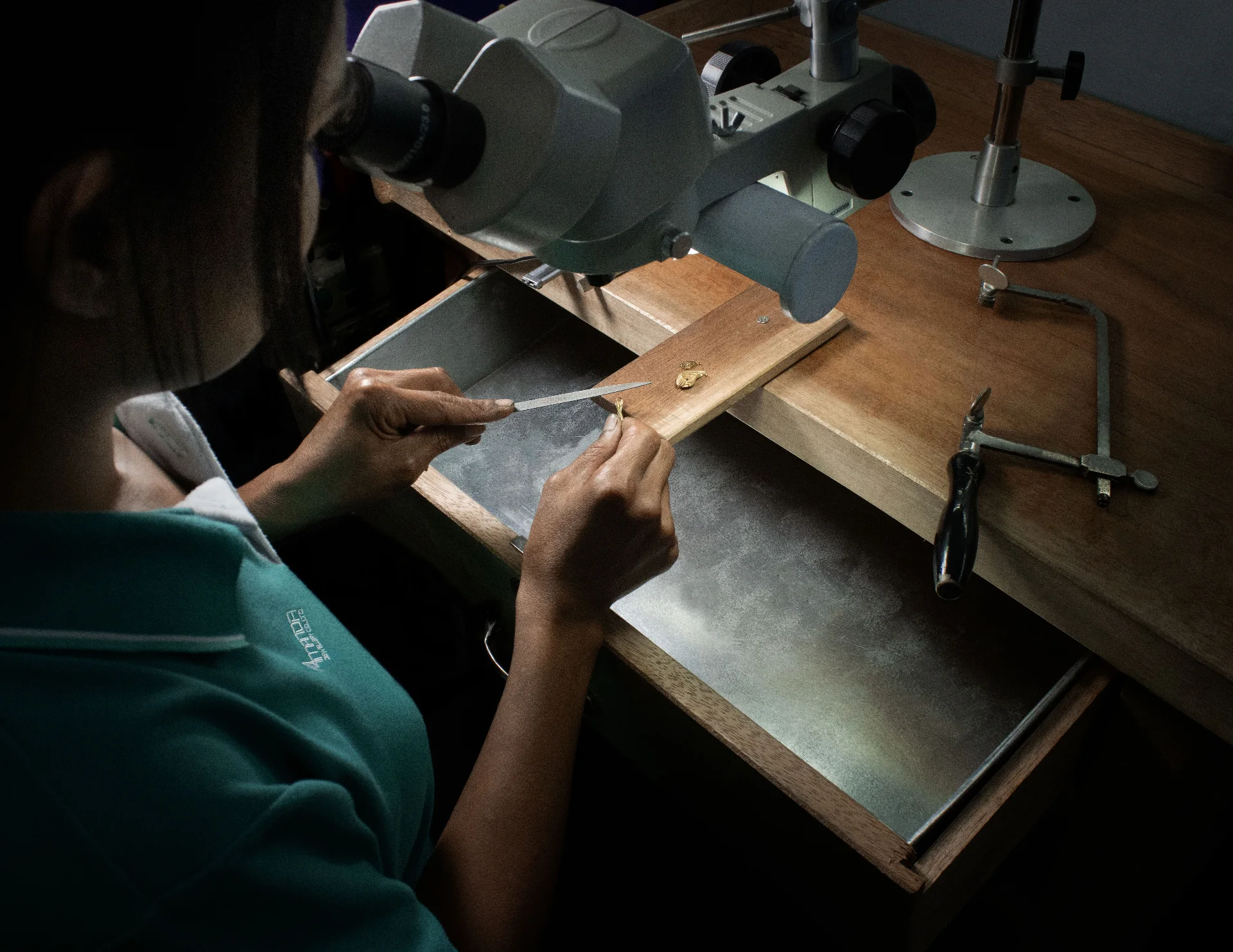 Amanda Jewellery craftsperson working under stereo microscope on a gold piece, Bangkok atelier
